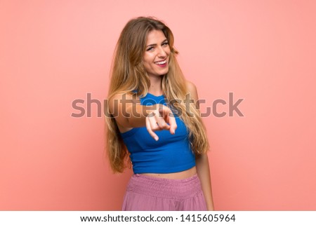 Young blonde woman over isolated pink background points finger at you with a confident expression
