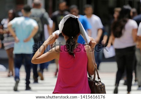 Woman protect herself from the hot sun while walks in a downtown street during an extreme heatwave in Sao Paulo, Brazil. Royalty-Free Stock Photo #1415616176