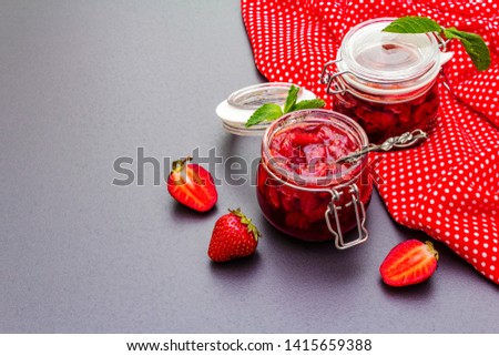 Strawberry jam in a glass jar. Homemade preservation concept. With fresh strawberries and mint, silver spoon on black stone background, polka dots cloth, copy space
