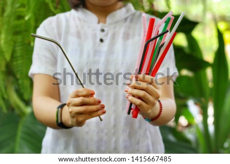 Asian girl show many plastic straws and one stainless straw in her hands with green garden background.Use steel tube for Replacement plastic,can save the earth.Reduce global warming concept. Royalty-Free Stock Photo #1415667485