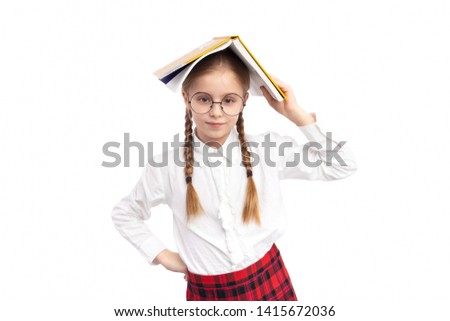 Confident nerdy girl in school uniform and glasses keeping open textbook on head and looking at camera against white background