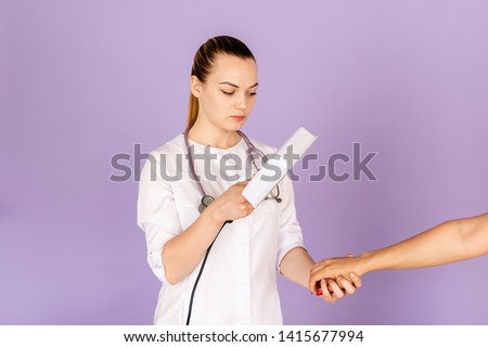 Young female doctor in white uniform with phonendoscope on her neck holding wood's light on purple background with space for text. Healthcare concept.