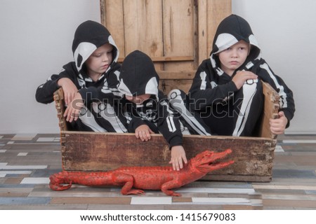 Happy children in carnival outfits, boys with a red crocodile in the studio. Black suit with the image of skeletons. Classic halloween costume. Funny family kids childhood