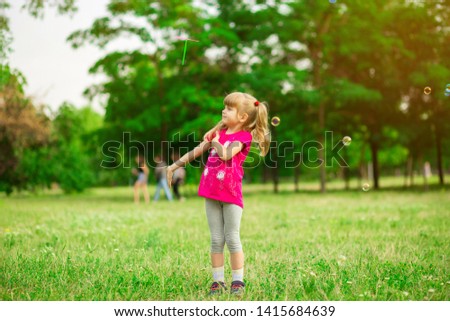 Little girl playing on the meadow on sun with windmill in her hands. Child holding wind toy on wheat field.