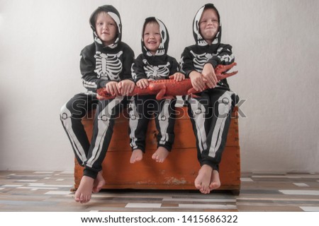 Happy children in carnival outfits, boys with a red crocodile in the studio. Black suit with the image of skeletons. Classic halloween costume. Funny family kids childhood