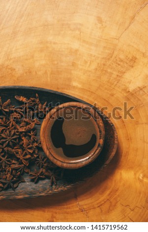 Black coffee in wooden cup with wooden spoon and star anise in a plate on wooden background. Close-up of espresso in brown cup with spoon and star anise . Image with film effect and author processing.