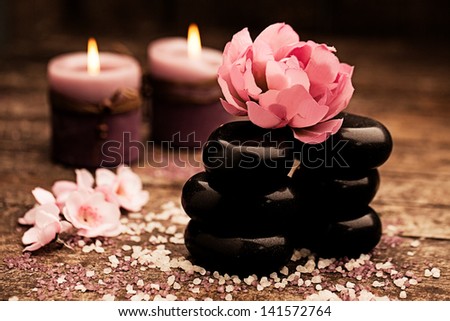 Spa still life composition of hot stones, a pink flower and candles.