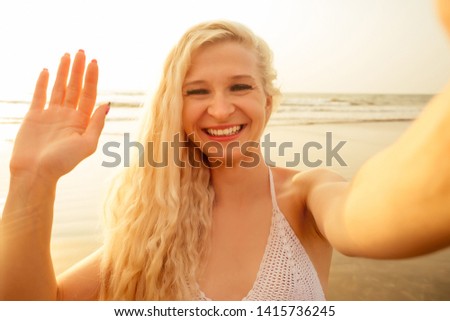 Close up of cheerful young girl in summer hat taking a selfie at the beach and sending air kiss hello hi