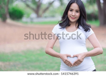 Portrait of asian Beautiful pregnant woman at the park,Thailand people,Happy woman concept,Her use hand touch her belly,She make hand shape heart