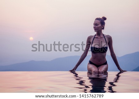 Young woman relaxing in infinity swimming pool looking at view romantic sunset overlooking the hills wildernest nature spa resort in India Goa Kerala