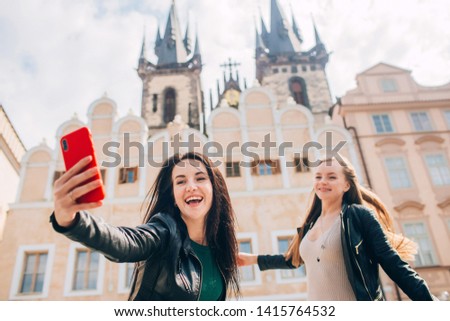 Cute girls take selfies. best friends are walking around Prague. Blonde and brunette enjoy traveling in Prague in the background Old Town Square. Closeup portrait. Woman makes the photo on the phone.