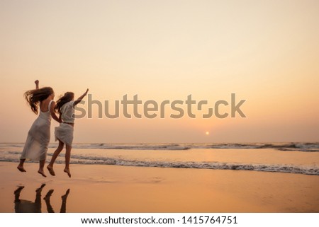 Happy mother and young daughter on the beach at sunset having fun at the seaside. playing jumping and rejoicing woman and her child copy space copyspace
