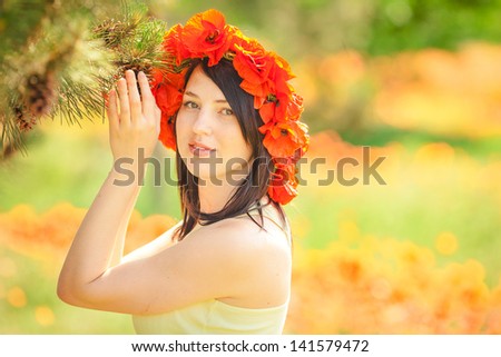 Beautiful woman in poppy wreath in summer poppy field. Outdoor portrait.