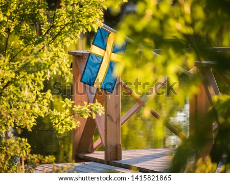 Swedish flag on a floating dock in summer sunset light in Sweden. Royalty-Free Stock Photo #1415821865