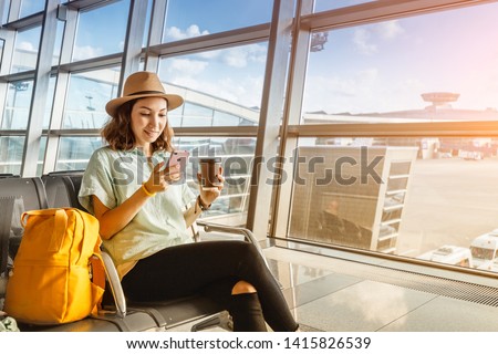 Asian girl waiting for departure at the airport on your vacation. Uses a smartphone and drinks coffee Royalty-Free Stock Photo #1415826539