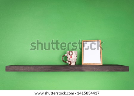 on the green wall there is a dark colored shelf with a mug and a photo frame on it