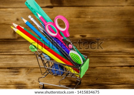 Buying school supplies. Shopping cart with school supplies on a wooden background. Back to school concept