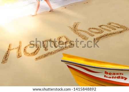 Hong Kong title on the sand beach of the South China sea. The red amber boat stands on the shore. A man walks along the coast.