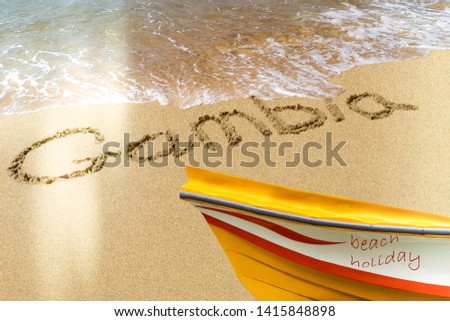 Gambia title on the sand beach Atlantic coast. The red boat stands on the shore.