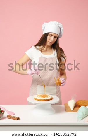 Chef cook confectioner or baker in white t-shirt, toque chefs hat cooking at table isolated on pink pastel background in studio. Cream application, cake making process. Mock up copy space concept