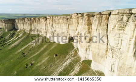Stunning landscape of White Rock in Crimea with bright green meadow at the foot. Shot. Aerial for the beautiful mountain with flat top and green field on cloudy sky background.