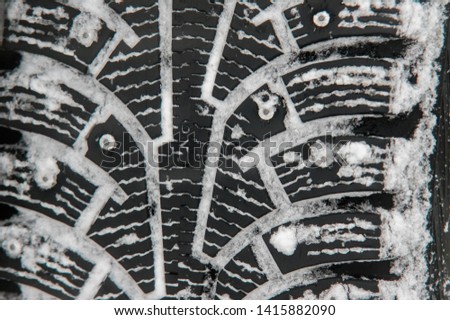 Winter tires close-up. Tread pattern filled with snow and small studs visible. Driving in slippery winter weather.