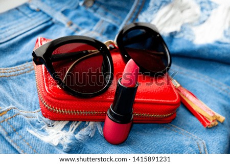 red wallet sunglasses and lipstick on blue jeans pants