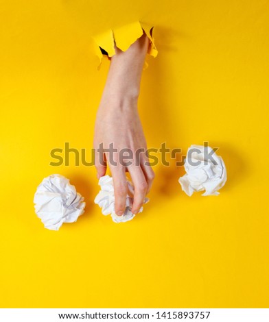 Female hand holds crumpled balls of paper through torn yellow paper. Minimalistic idea business concept