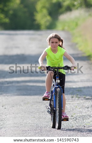 Girl teens in neon yellow shirt riding a bicycle down an old forest road