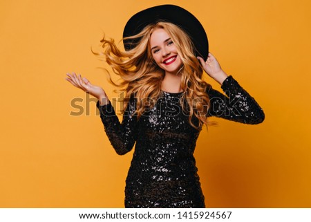Carefree long-haired woman in hat laughing to camera. Good-humoured white lady with curly hair expressing happiness.