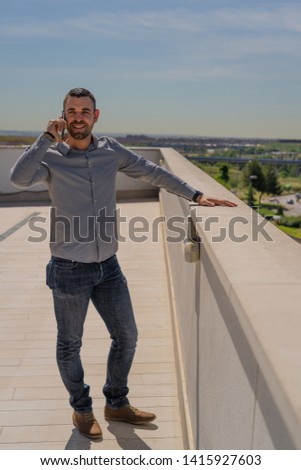 young pretty man talking on mobile phone on a rooftop or terrace, blue sky