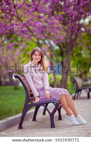 Young beautiful woman in a pink dress sitting on the bench. Spring outdoors park. 