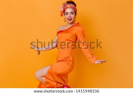 Blue-eyed bright lady in massive earrings and orange elegant dance dress on isolated background