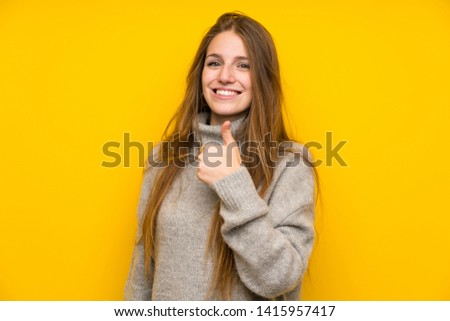 Young woman with long hair over yellow background giving a thumbs up gesture