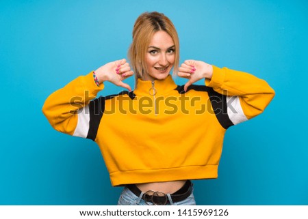 Young blonde woman over isolated blue background proud and self-satisfied