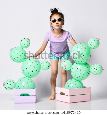 Young asian girl hold cactus balloon in pastel pink and purple flower box made of green round balloons with pink flowers. Creative idea minimal concept on gray background