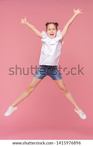 Funny little girl laughing, jumping on pink background and enjoying life