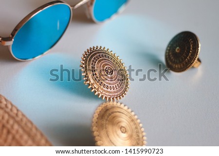 Close-up of a gorgeous vintage earrings with beautiful ornaments made in India. Placed between ring, straw hat and sunglasses with blue reflection. Still Photography