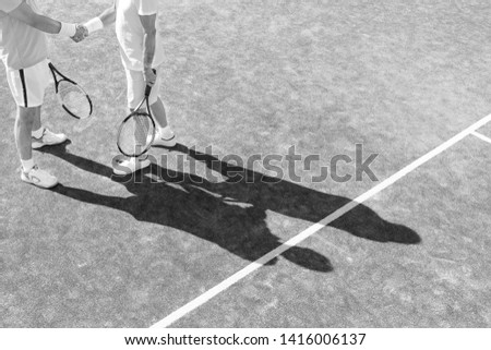 Black and White photo of Low section of mature men shaking hands while standing on tennis court during match