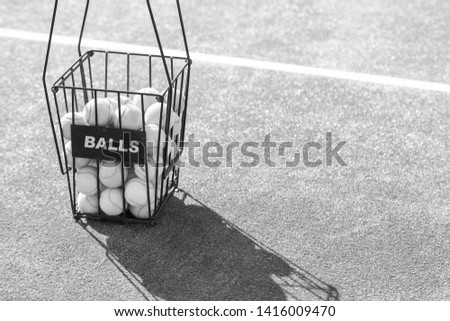 Black and White photo of High angle view of balls in metallic basket with label on tennis court