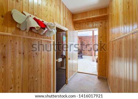 Corridor in front of the entrance to the bath with wooden walls, hanging on the hooks hats for bath