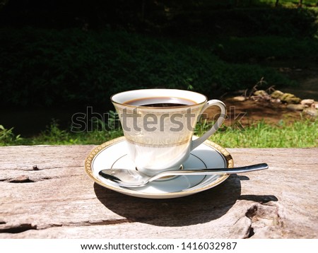 White coffee cup with spoon on the wooden table beside the waterfalls, The combination of coffee in the nature concept.