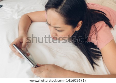 Upset Asian woman is playing mobile game on her bed.