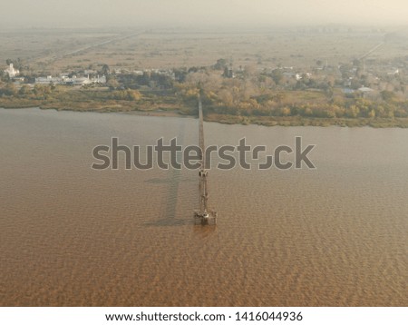 Aerial view of the coast with few buildings, large amount of trees and a very long dock for fishermen, in a very wide river in Argentina.