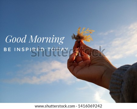 Morning inspirational quote- Good morning. Be inspired today. With blurry image of  young woman hands holding sea weed against the bright and blue sky on a sunny day welcoming summer season. 