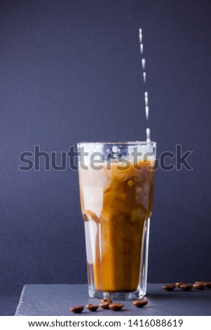 Iced coffee with milk on a dark background. Summer drink with caffeine on the slate board. Latte in a glass cup and coffee beans. Copy space