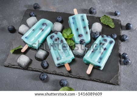 Blue popsicles with blueberries on dark background