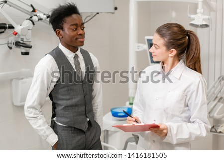 African male patient in dental clinic. Young Woman dentist makes a diagnosis and records recommendations. Medicine, health, stomatology concept. dentist treating a patient.