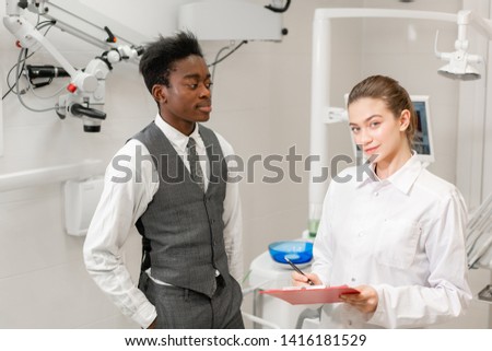 Young Woman dentist makes a diagnosis and records recommendations. African male patient in dental clinic. Medicine, health, stomatology concept. dentist treating a patient.