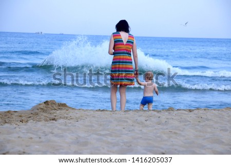 Mother and son watch the sea together. Mom holds hand of her child. Back view. Summer sea vacation concept. Royalty-Free Stock Photo #1416205037